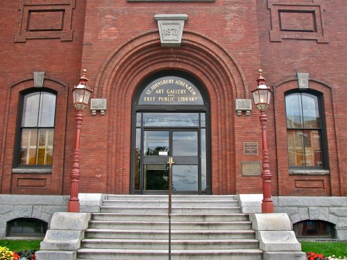 Entrance of a historic brick building featuring arched windows, steps, and decorative lampposts.