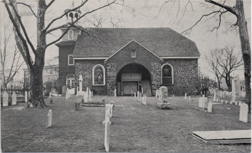 Historic stone church surrounded by a graveyard, with trees and tombstones visible in a black-and-white photo.