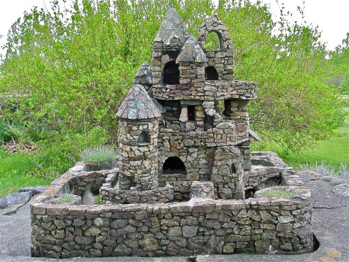 A small stone castle structure with turrets, surrounded by greenery and a stone wall.