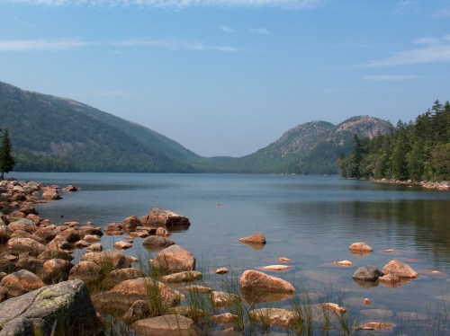 A serene lake surrounded by mountains, with rocky shores and calm waters reflecting the blue sky.