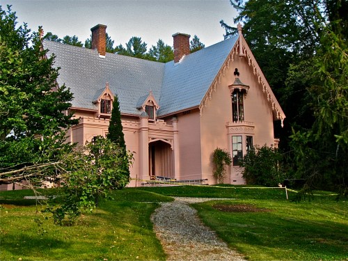 A pink Gothic-style house surrounded by greenery, with a gravel path leading to the entrance.