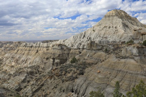 A rugged landscape featuring layered rock formations under a cloudy sky, showcasing natural erosion and geological features.