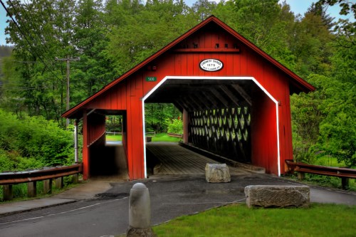 A red covered bridge surrounded by lush greenery, with a stone entrance and a sign above the archway.