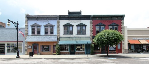 A row of colorful, historic buildings with varied architectural styles and a tree in front, set against a clear sky.