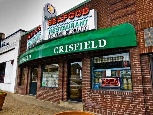 Exterior of Crisfield Seafood Restaurant, featuring a green awning, neon "OPEN" sign, and a vintage seafood sign.