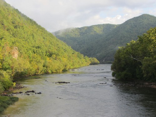 A serene river flows through lush green mountains under a partly cloudy sky.