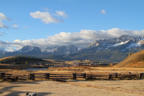 A scenic landscape featuring mountains, a clear sky, and a grassy field with wooden fences in the foreground.