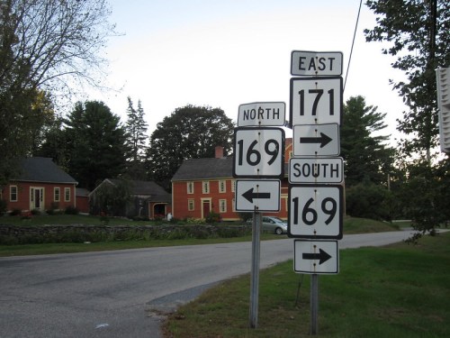Road signs indicating directions for routes 169 and 171, with a rural house in the background.
