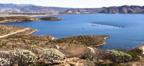 A scenic view of a blue lake surrounded by hills and greenery under a clear sky.