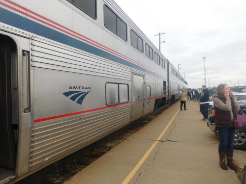 Amtrak train at a station with passengers boarding and waiting on the platform. Cloudy sky in the background.