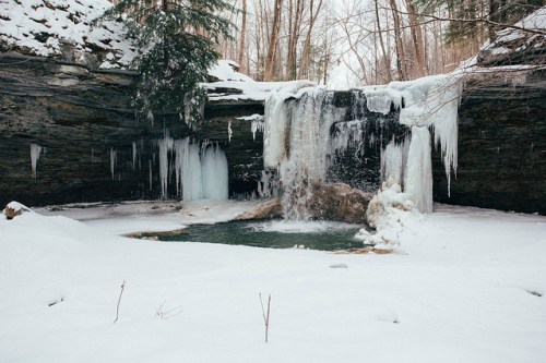 A frozen waterfall surrounded by snow-covered rocks and trees, creating a serene winter landscape.