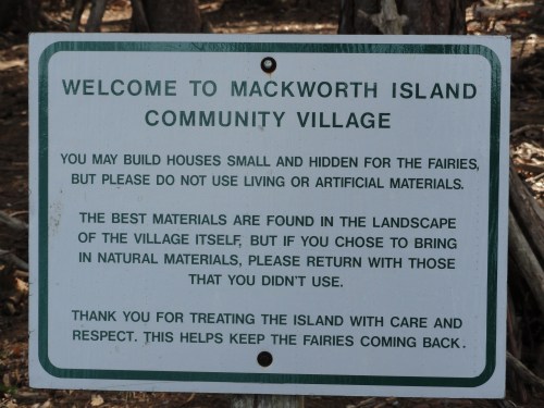 Sign welcoming visitors to Mackworth Island Community Village, emphasizing care for fairies and natural materials.