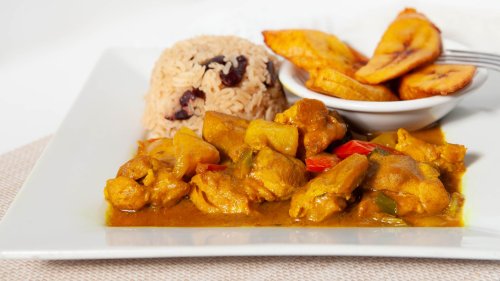 A plate of curry chicken with rice and beans, accompanied by fried plantains.