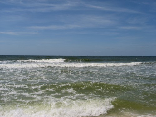 Waves gently roll onto a sandy beach under a clear blue sky, creating a serene coastal scene.