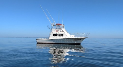 A white fishing boat named "Slipper" floats on calm blue waters under a clear sky.