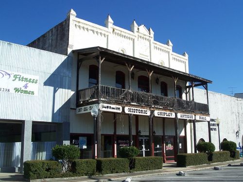 Historic Chipley Antique Mall building with a balcony, flanked by modern storefronts under a clear blue sky.