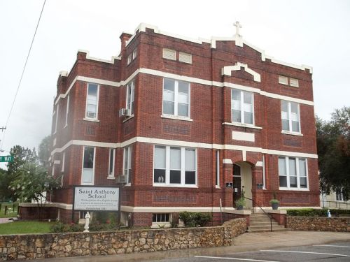 Brick building with a cross on top, featuring large windows and a sign for Saint Anthony School.