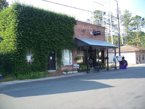 A brick building covered in green ivy, featuring a covered entrance and a sign, set on a quiet street.