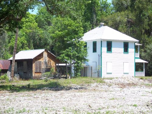 Two houses side by side: a wooden cabin and a two-story white house, surrounded by greenery and trees.