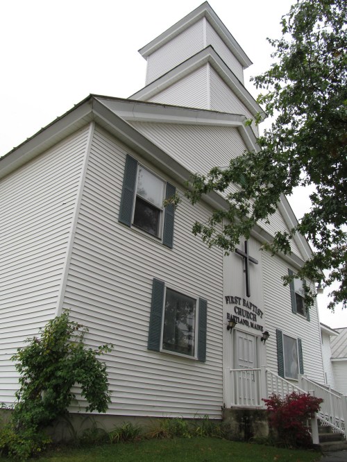 Exterior view of First Baptist Church in Houlton, Maine, featuring a white facade and a prominent cross.
