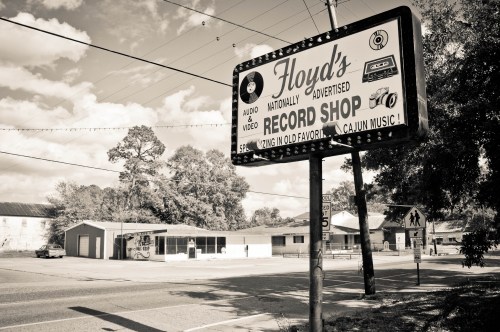 Black and white image of a vintage sign for Floyd's Record Shop, with a small building in the background.
