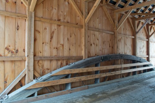 Interior of a wooden barn with a sloped roof and wooden beams, featuring a curved wooden structure against the wall.