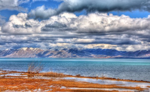 A serene landscape featuring a lake, mountains in the background, and dramatic clouds overhead.