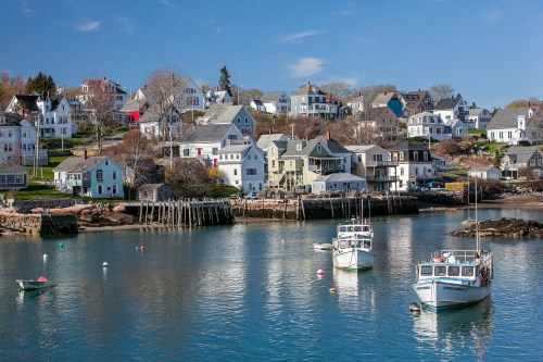 A serene coastal scene with boats in the water and charming houses on a hillside under a clear blue sky.
