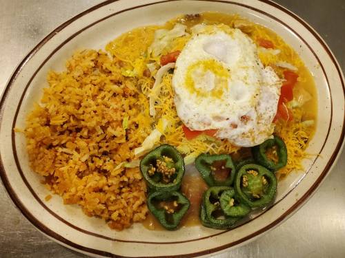 A plate of rice, topped with lettuce, tomatoes, cheese, two fried eggs, and sliced jalapeños.