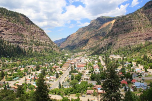 A scenic view of a valley town surrounded by mountains, with greenery and a clear blue sky.