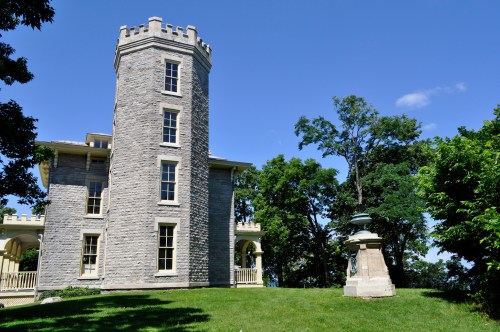 A stone tower building with a turret, surrounded by trees and a grassy area under a clear blue sky.