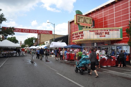 A bustling street scene at the Traverse City Film Festival, with tents, vendors, and the State Theatre marquee in view.