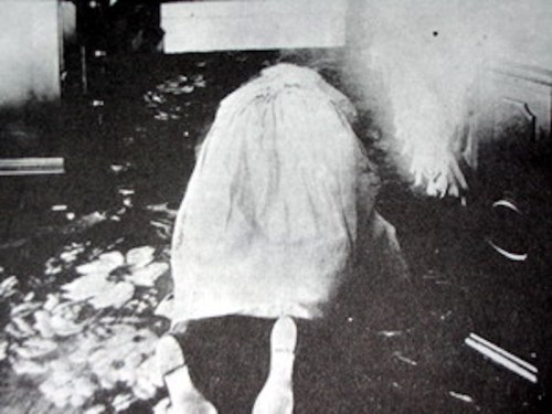 A black and white image of a figure on the floor, partially covered, with a blurred background.