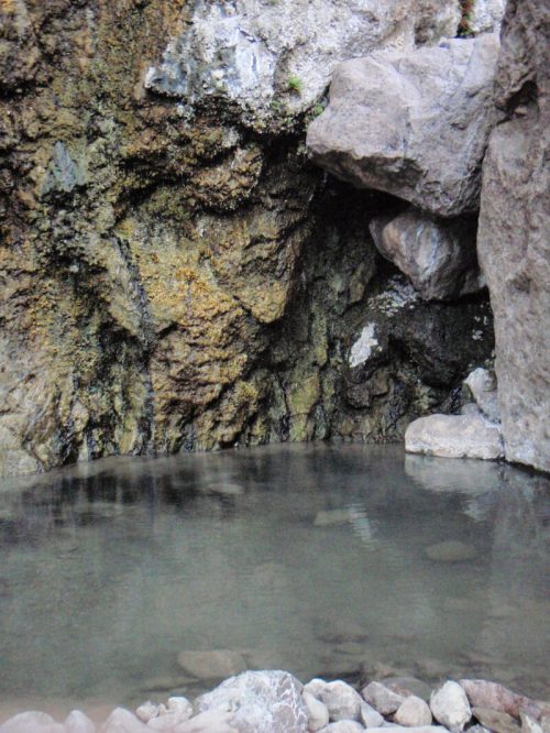 A serene natural pool surrounded by rocky terrain, with clear water reflecting the surrounding stones.