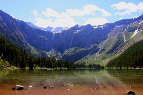 A serene mountain lake surrounded by lush forests and towering peaks, with waterfalls cascading in the background.