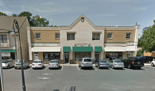 A small commercial building with green awnings, featuring several storefronts and parked cars in front.