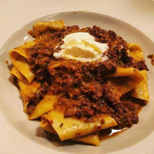 A plate of pappardelle pasta topped with a rich meat sauce and a dollop of creamy sauce.