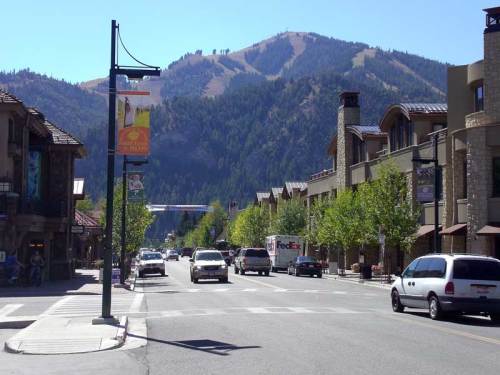 A street lined with trees and buildings, with mountains in the background under a clear blue sky.