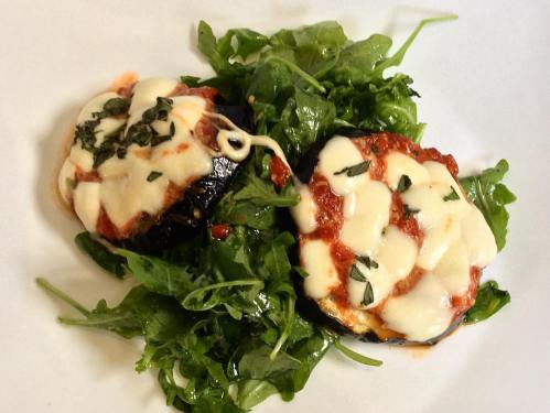 Two baked eggplant rounds topped with marinara sauce and melted cheese, served on a bed of fresh arugula.