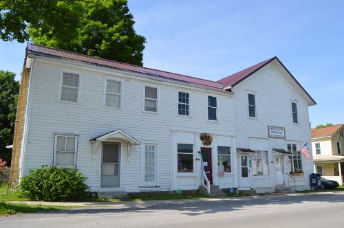 A two-story white building with a red roof, featuring a barbershop sign and an American flag outside.