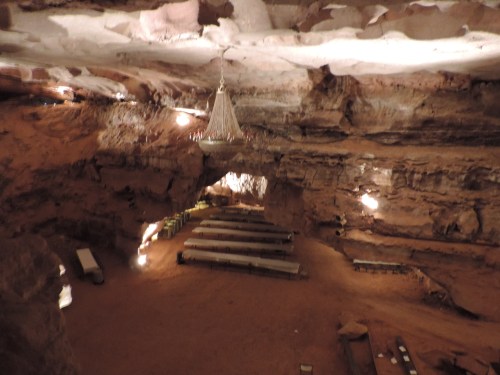 A spacious cave interior with a chandelier, featuring rows of tables and warm lighting illuminating the rocky walls.