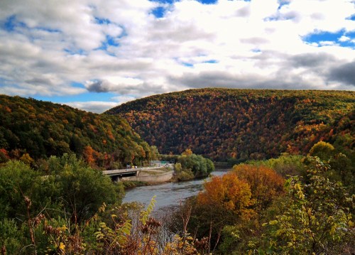 A scenic view of a river winding through colorful autumn hills under a partly cloudy sky.