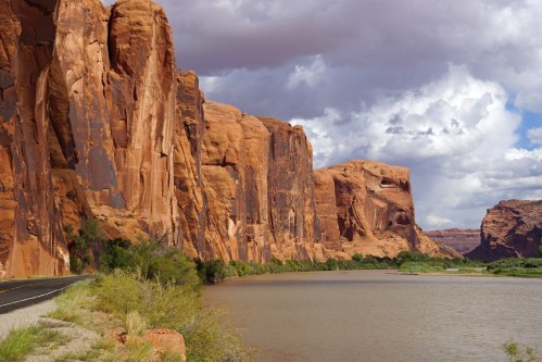 A scenic view of red rock cliffs alongside a river under a cloudy sky.