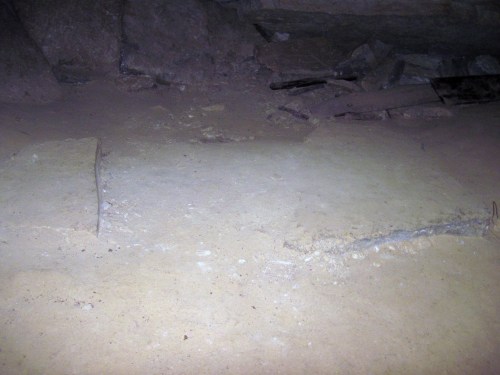 A dimly lit cave floor with uneven stone surfaces and scattered debris.
