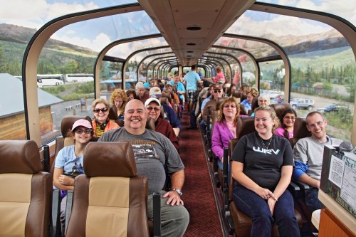A group of smiling passengers seated in a scenic train car, enjoying a journey through beautiful landscapes.