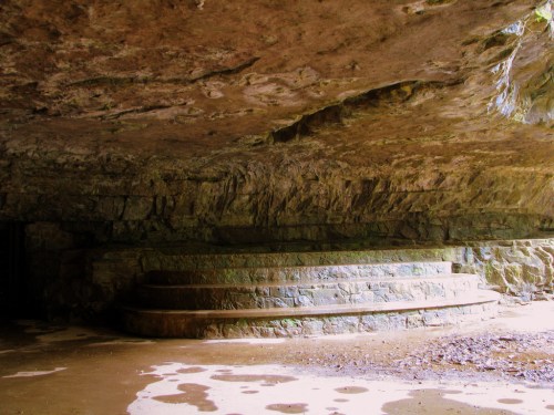 A stone structure with tiered steps under a rocky overhang, surrounded by natural rock formations.