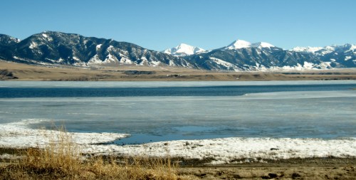 A serene landscape featuring a frozen lake with snow-capped mountains in the background under a clear blue sky.