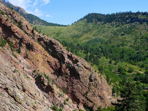 A rocky hillside with vibrant colors, surrounded by lush green mountains and a clear blue sky.