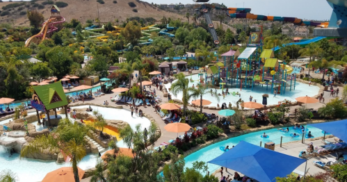 A vibrant water park scene with slides, pools, and families enjoying the sunny day under colorful umbrellas.