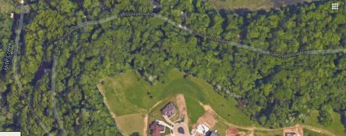 Aerial view of a wooded area with a winding road and a few residential properties near a creek.